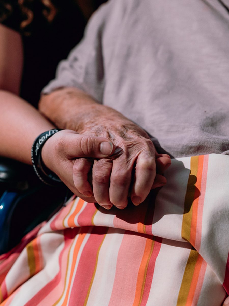 A caregiver holding the hand of an elderly hospice patient